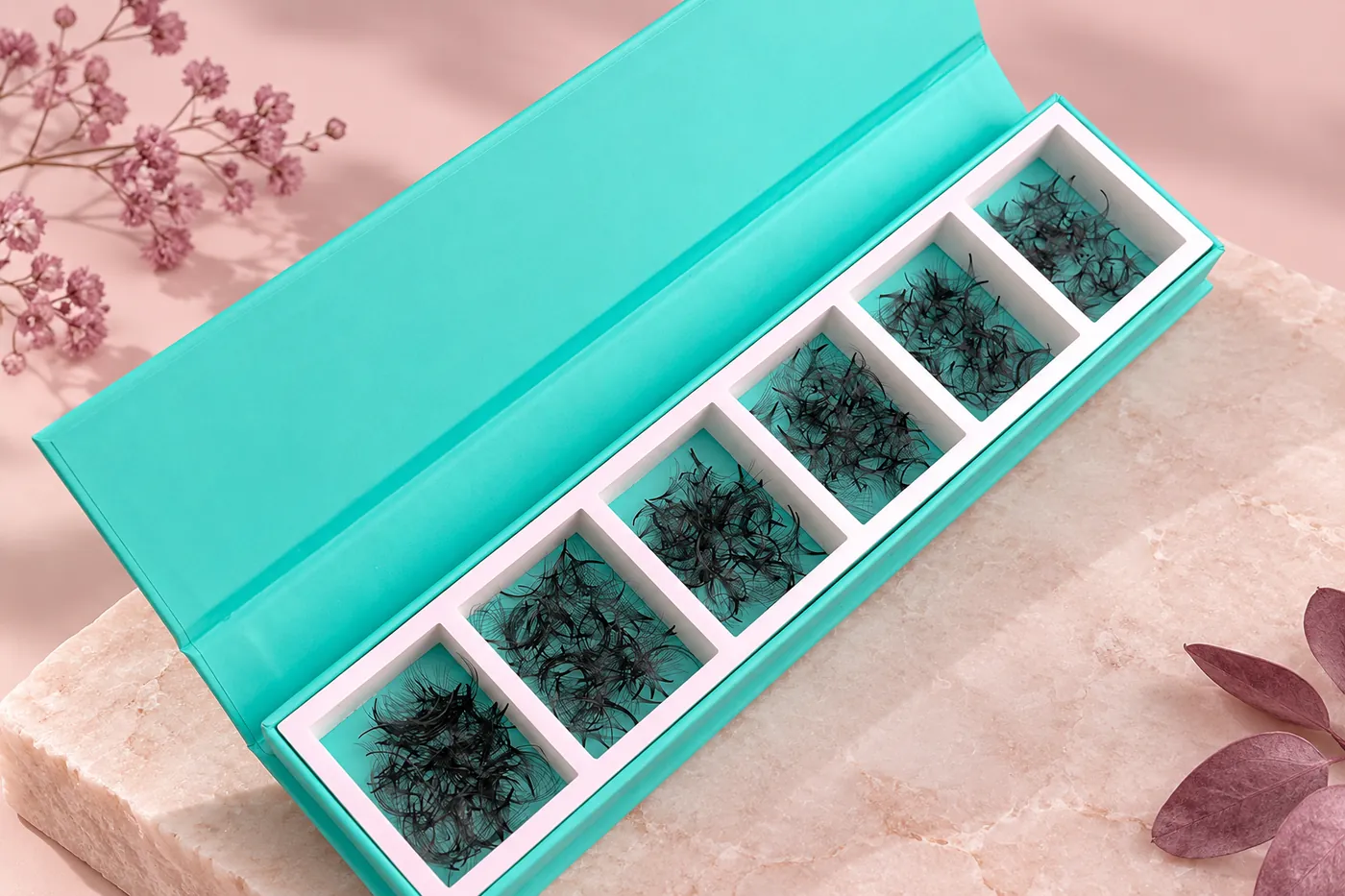 Turquoise divided carton containing loose black premade lash fans