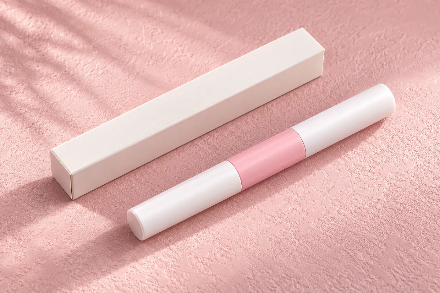 Closed pink-and-white dual-ended tube beside a plain narrow unprinted carton