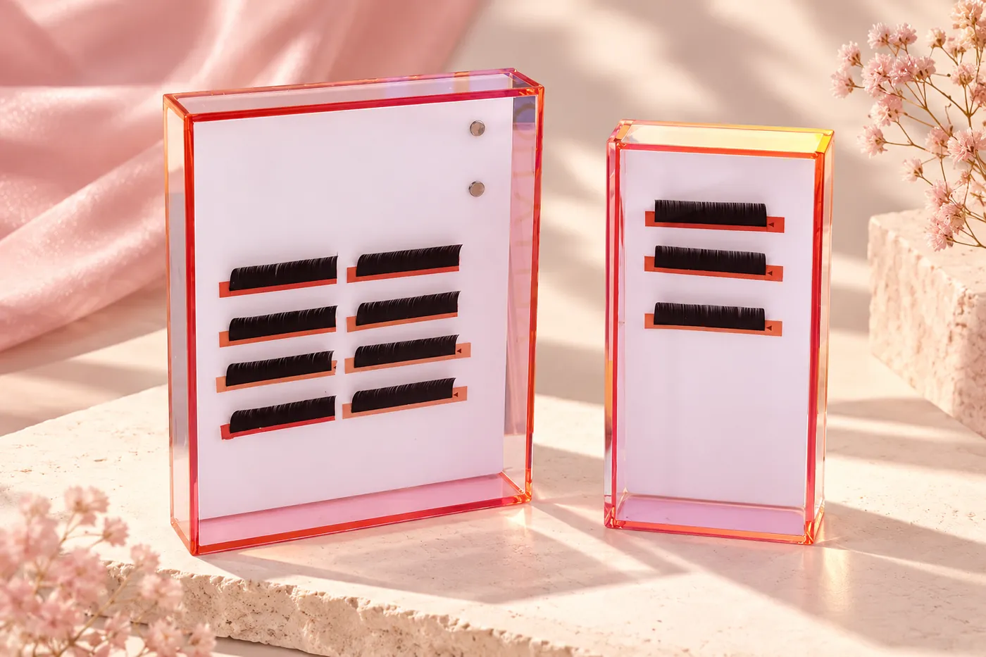 Two clear covered acrylic lash tile cases with pale inserts and short lash strips