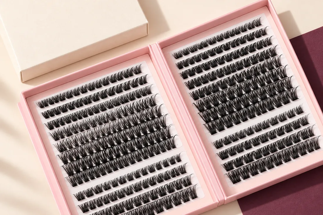 Top-down view of an open pink cluster lash book with an unprinted cream sleeve beside it